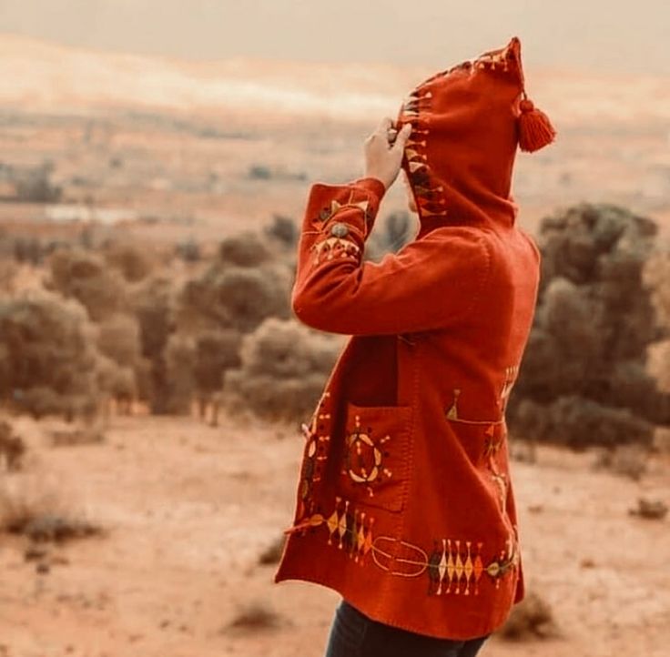 a person outside in red that is looking back into an arid landscape